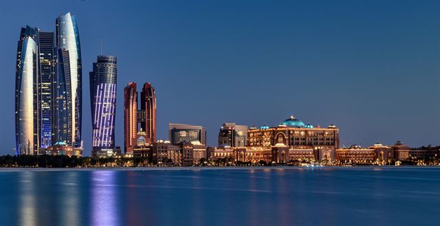 Abu Dhabi skyline with the Etihad Towers lit up across the water at dusk, United Arab Emirates