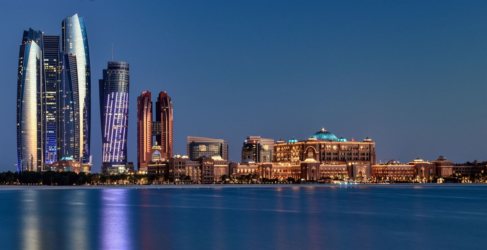 Abu Dhabi skyline with the Etihad Towers lit up across the water at dusk, United Arab Emirates