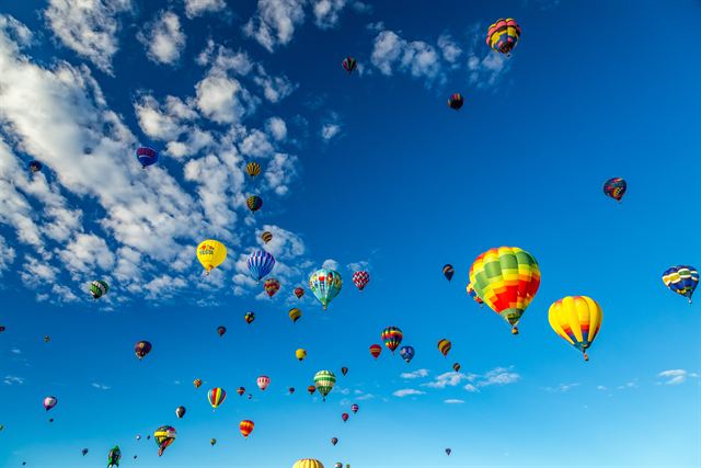 Colorful hot air balloons drifting across a blue sky during the Albuquerque Balloon Fiesta