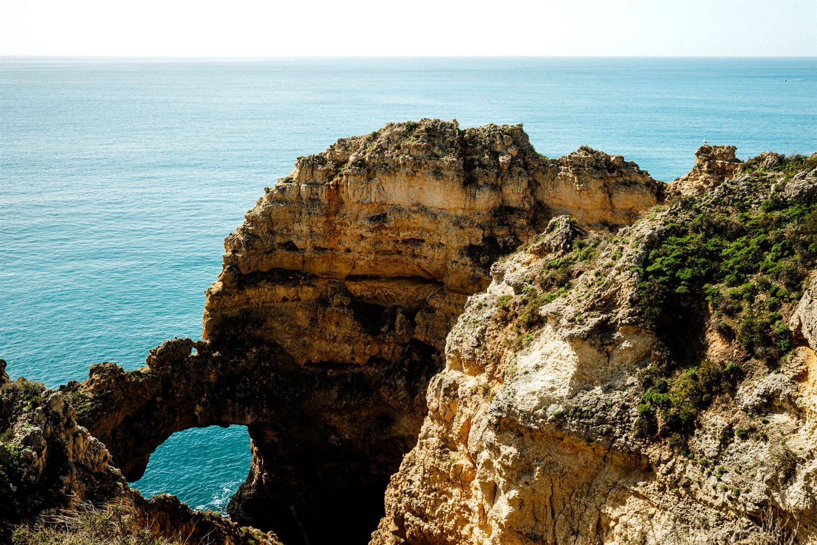 Golden limestone cliffs and a natural sea arch above turquoise Atlantic water on the Algarve coast
