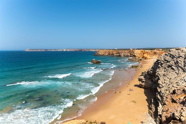 Sagres beach in the Algarve, a sandy cove below tall cliffs with rolling Atlantic surf