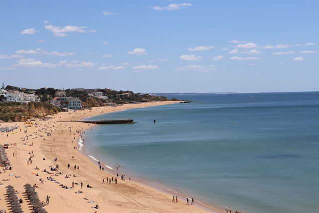 Long sandy Algarve beach with umbrellas, sunbathers and whitewashed hillside town on a sunny day
