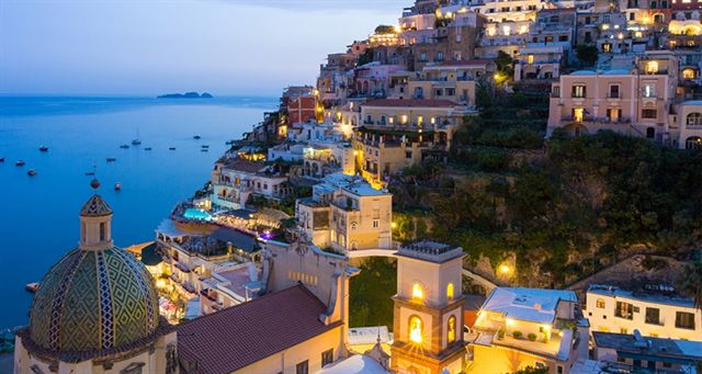 Positano at dusk with the tiled dome of Santa Maria Assunta and hillside houses above the sea
