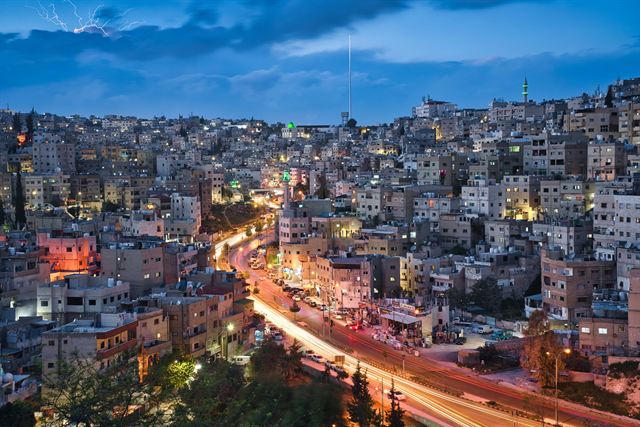 Hillside houses of Amman glowing at sunset with traffic lights streaking through the valley, Jordan