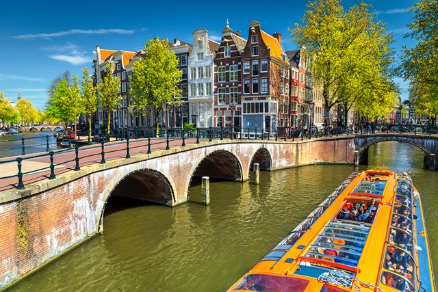 Canal tour boat passing under an arched bridge lined with gabled canal houses