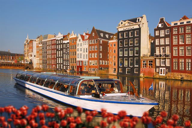 Glass-roofed canal boat in front of colorful gabled canal houses