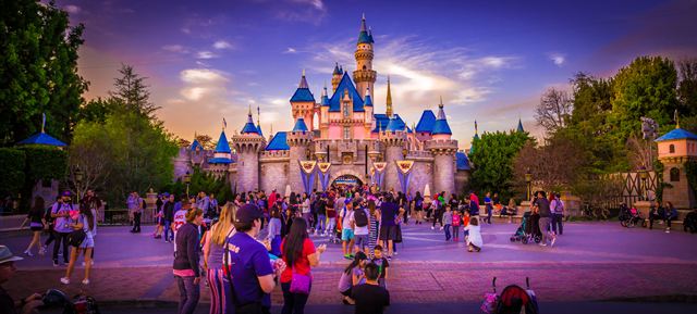 Sleeping Beauty Castle lit at dusk with visitors at Disneyland in Anaheim, California