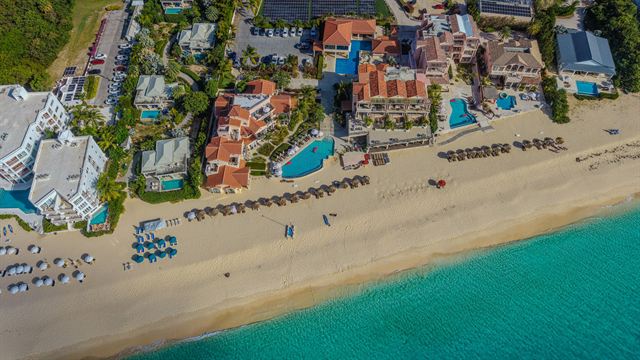 Aerial view of a white-sand Anguilla beach with beachfront resort buildings, pools and sun loungers