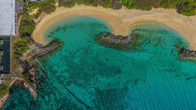 Aerial view of a curved sandy cove with rocky breakwaters and clear turquoise water in Anguilla