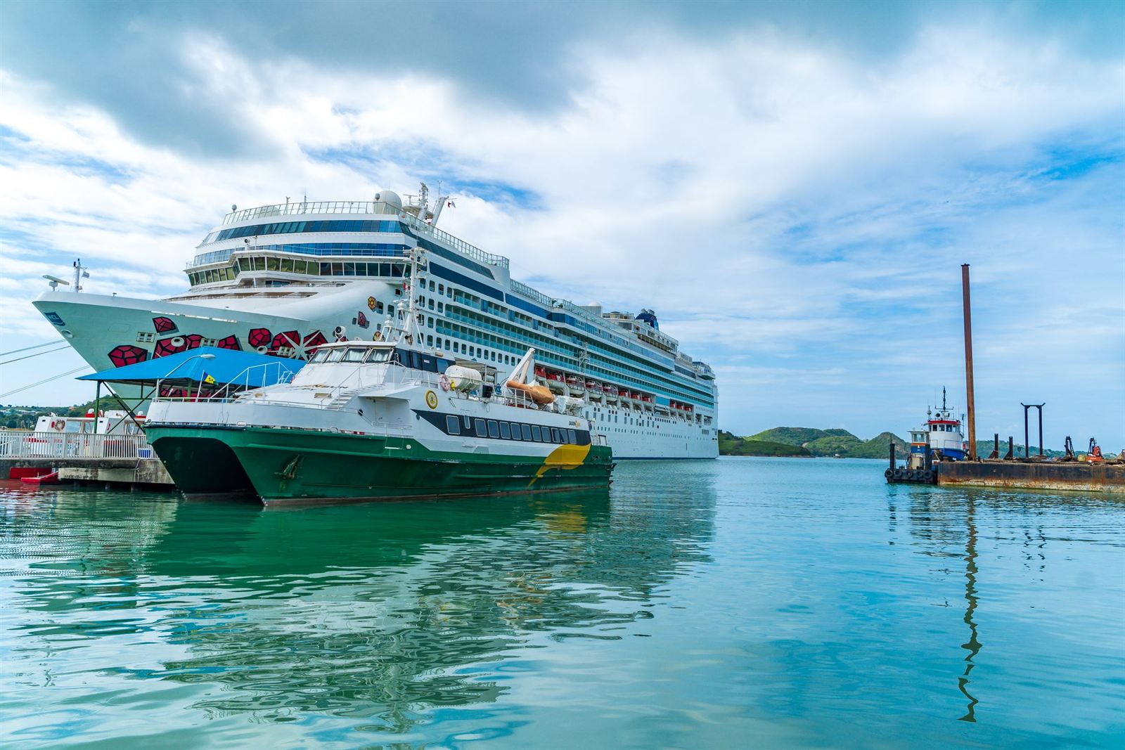 Cruise ship and green-hulled ferry docked in the turquoise harbor at St. John's, Antigua under a blue sky