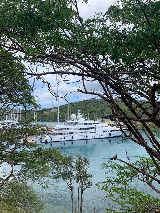 Superyacht moored in the calm blue water of English Harbour, Antigua, framed by tropical trees