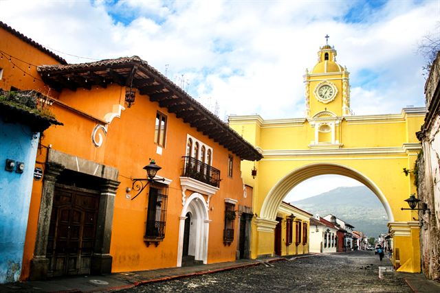 Yellow Santa Catalina Arch with its clock tower spanning a cobbled street of colorful colonial houses in Antigua Guatemala