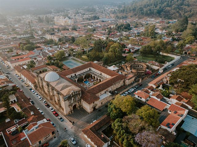 Aerial view of Antigua Guatemala's colonial rooftops, domed church and courtyards spreading toward green hills