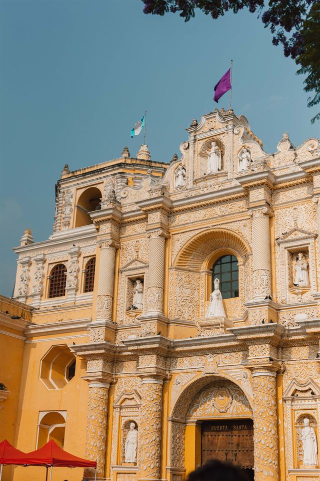 Ornate yellow and white Baroque facade of La Merced church in Antigua Guatemala under blue sky