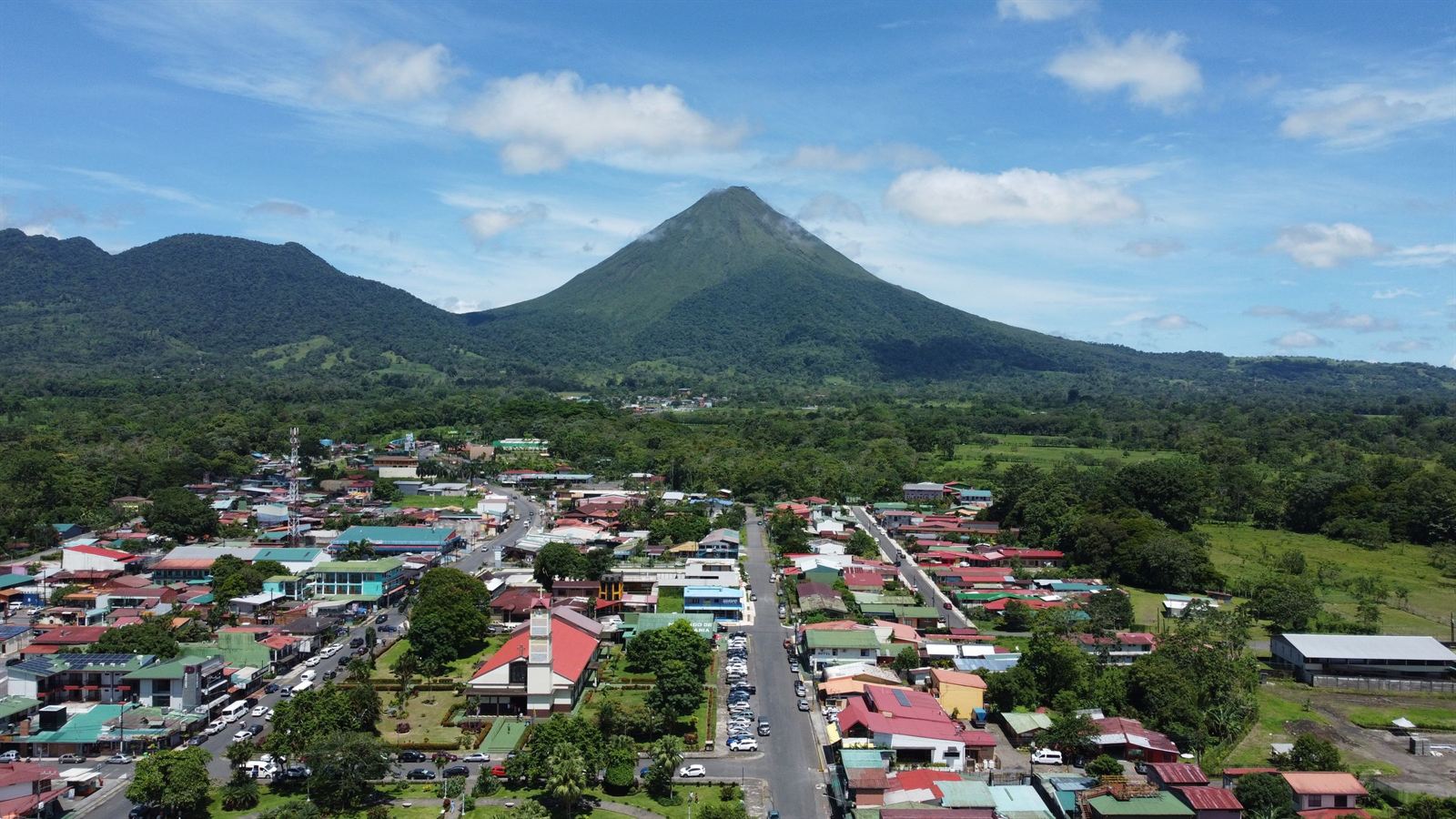 Aerial view of La Fortuna town's streets and rooftops with the green cone of Arenal Volcano rising behind