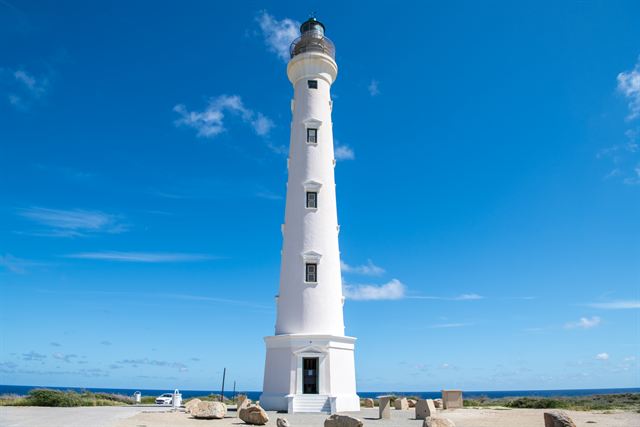 Tall white California Lighthouse against a deep blue sky on Aruba's northwest tip
