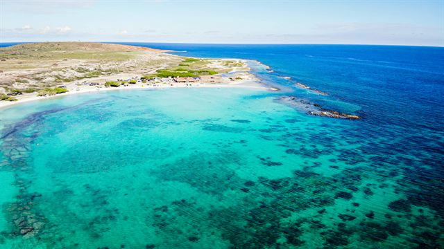 Aerial view of Baby Beach's shallow turquoise lagoon and sandy point in southern Aruba