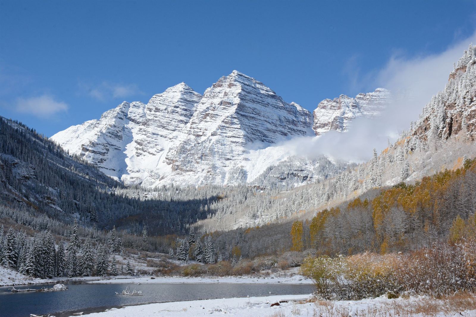 Snow-covered Maroon Bells peaks above a valley and lake near Aspen, Colorado in early autumn