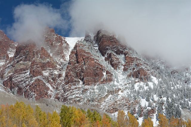 Snow-dusted red rock peaks of the Rockies above golden autumn aspens near Aspen, Colorado