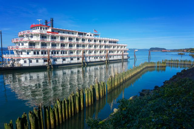 Sternwheeler cruise ship at an Astoria dock with the Columbia River estuary behind