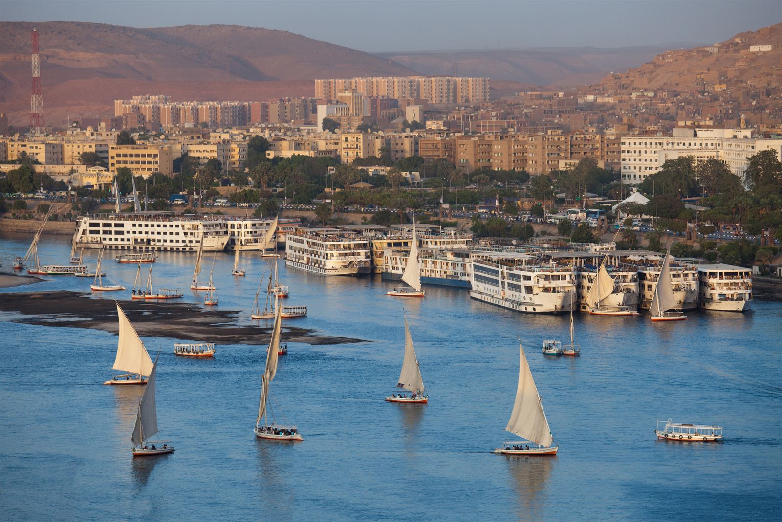 Aswan riverfront with feluccas sailing and Nile cruise ships moored below the town