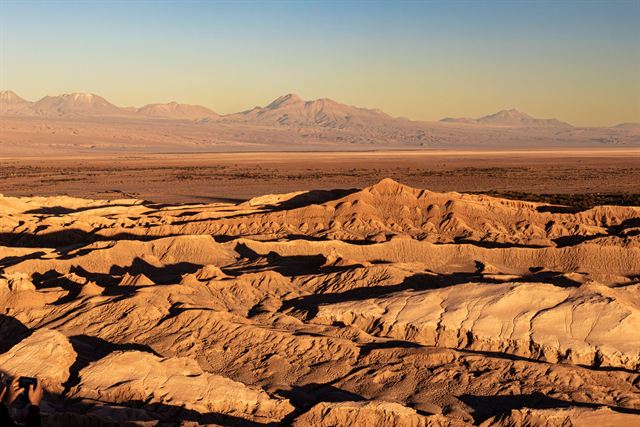Eroded salt and clay ridges of the Atacama Desert glowing at sunset with distant mountains