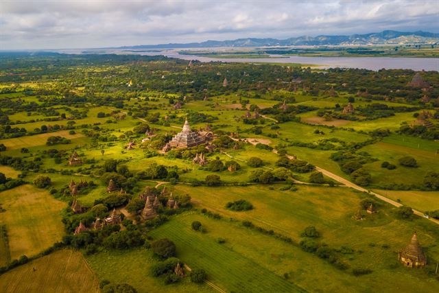Aerial view of the green Bagan plain dotted with ancient pagodas and the Irrawaddy river beyond