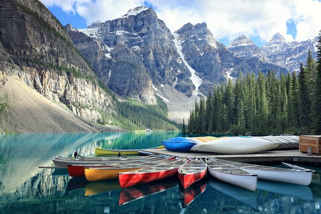 Row of colorful canoes at the Moraine Lake jetty beneath jagged peaks in Banff National Park