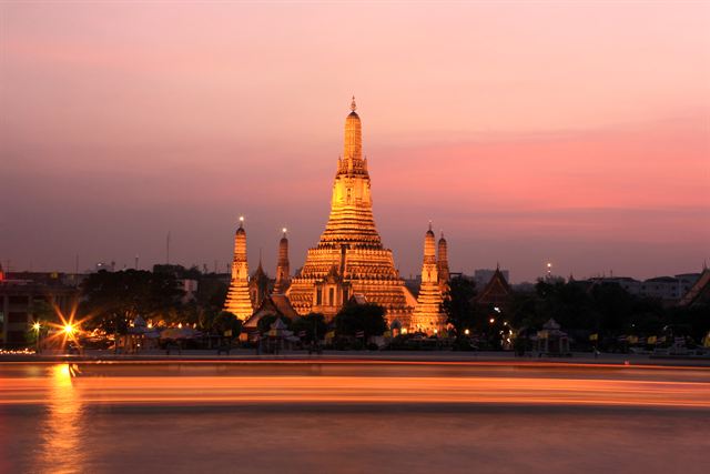 Wat Arun temple lit at dusk across the Chao Phraya River