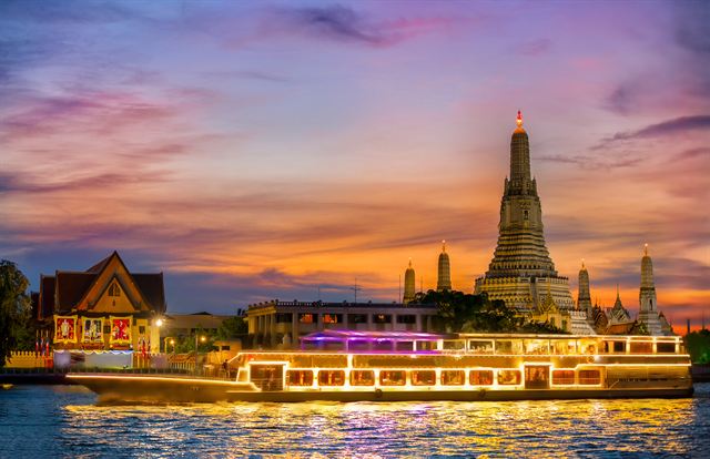Illuminated river dinner cruise boat passing Wat Arun at sunset