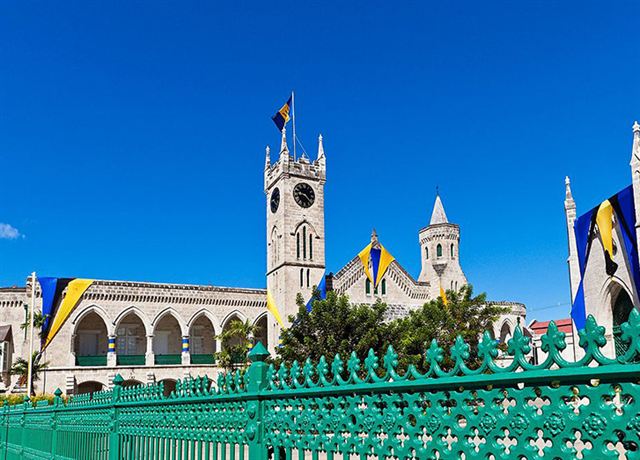 Neo-Gothic Parliament Buildings clock tower and Barbados flags behind a green railing in Bridgetown