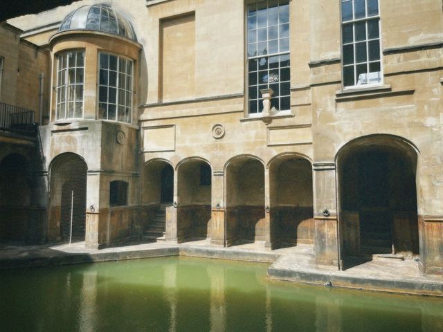 Green water of the Roman Baths in Bath framed by honey-colored stone arches and windows