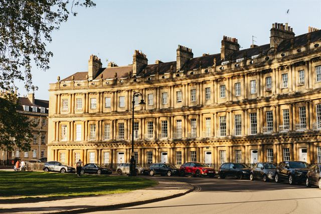 Sunlit honey-stone Georgian townhouses of The Circus in Bath with cars parked below
