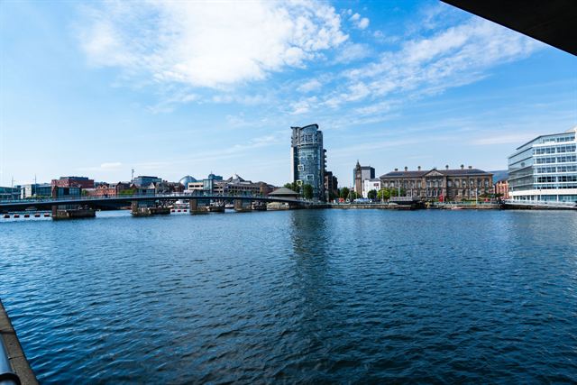 River Lagan waterfront in Belfast with the Obel Tower and city buildings under blue sky