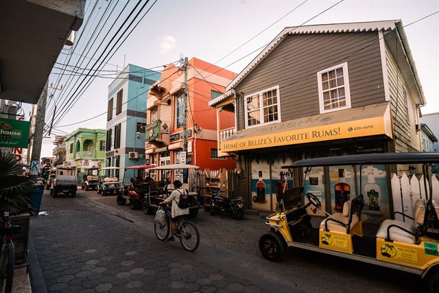 Colorful wooden buildings, golf carts and a cyclist on a street in San Pedro town, Ambergris Caye, Belize