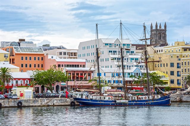 Tall ships moored on Hamilton's Front Street harbourfront below pastel buildings and the cathedral tower, Bermuda