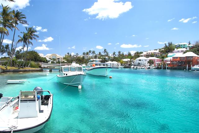 Motorboats in a turquoise cove below palms and white-roofed Bermuda houses near Hamilton