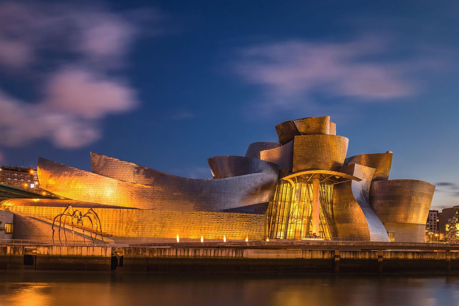 Guggenheim Museum Bilbao's titanium curves lit gold at dusk beside the Nervion river