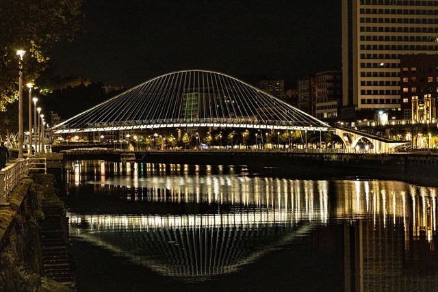 Zubizuri footbridge over the Nervion river in Bilbao illuminated and reflected at night