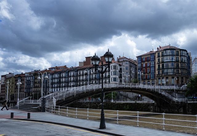 Historic Bilbao riverfront buildings with glassed balconies and an arched bridge over the Nervion