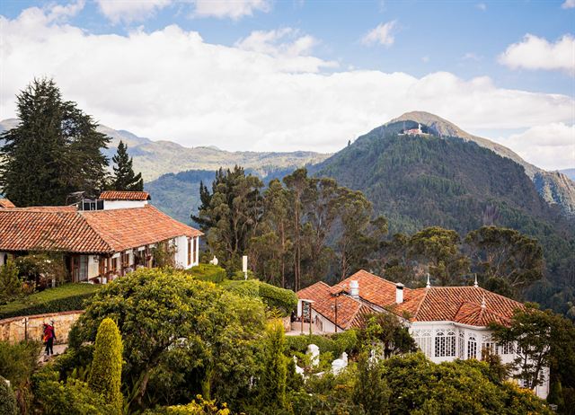 Red-tiled colonial buildings among gardens on Monserrate with the green Andes peaks of Bogota behind