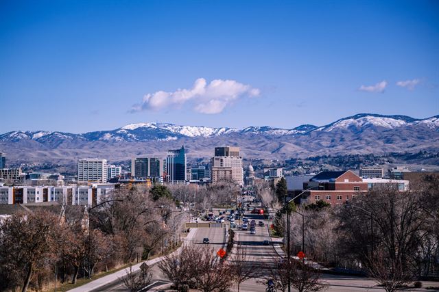 Downtown Boise skyline and a tree-lined boulevard with snow-dusted foothills behind under blue sky