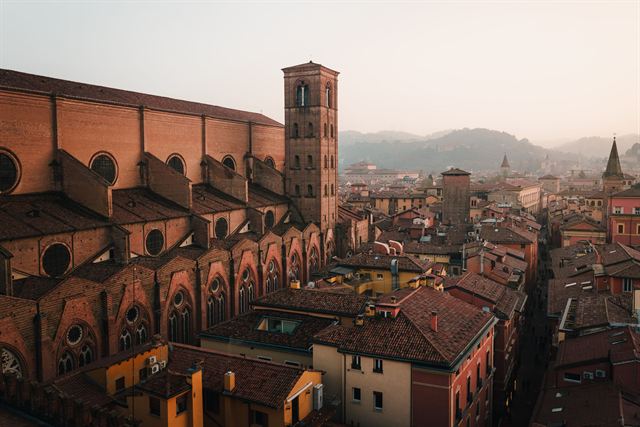 Basilica of San Petronio's brick flank and bell towers above Bologna's terracotta rooftops, hills in distance