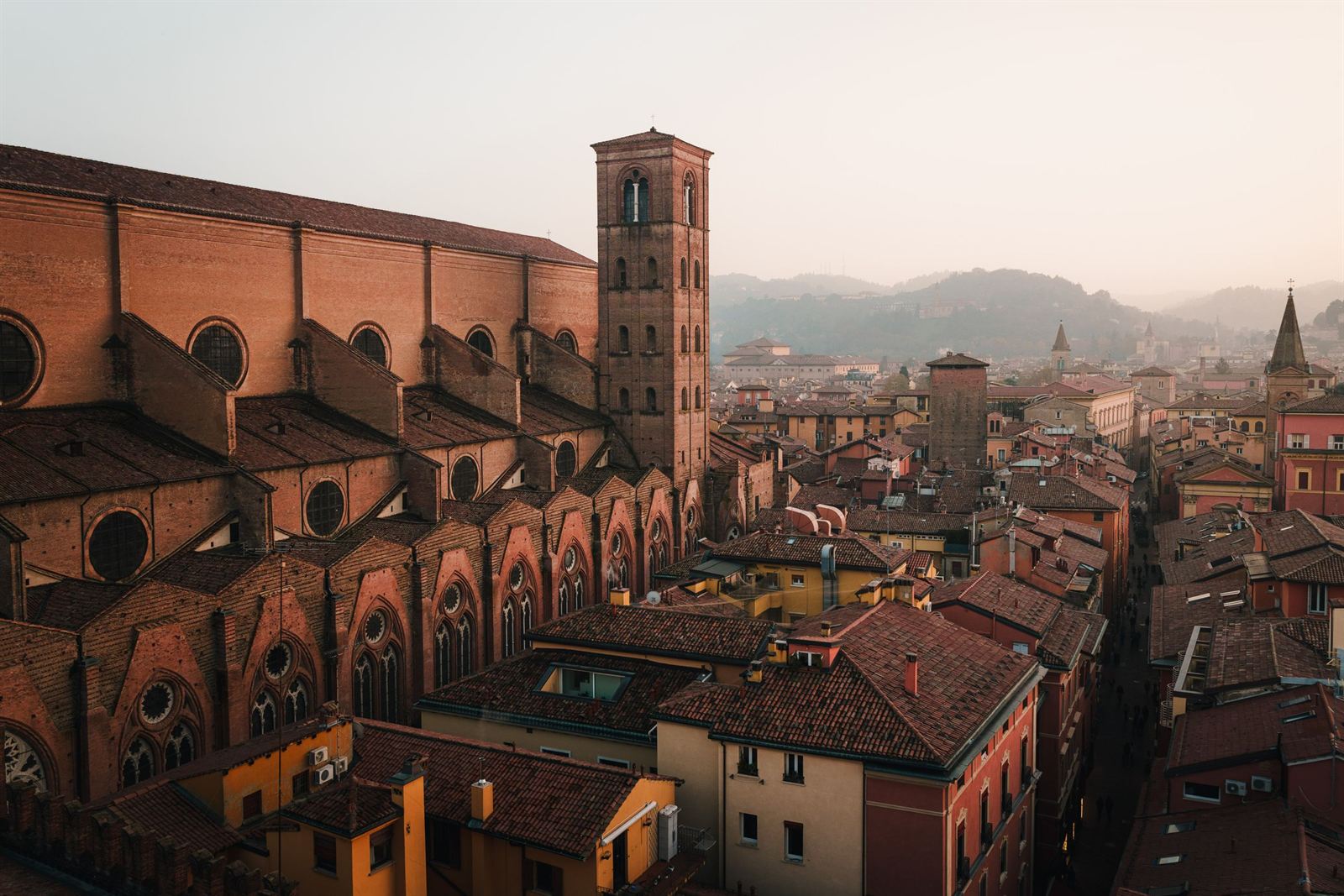 Basilica of San Petronio's brick flank and bell towers above Bologna's terracotta rooftops, hills in distance