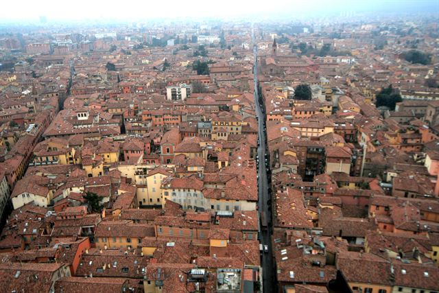 Aerial view straight down over Bologna's dense red-tiled rooftops and a long straight medieval street