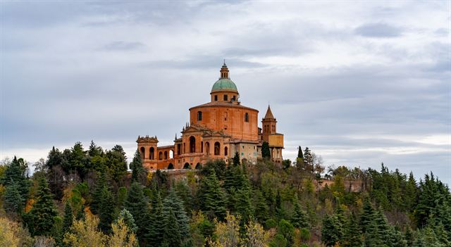 Sanctuary of the Madonna di San Luca crowning a wooded hill above Bologna under cloudy sky