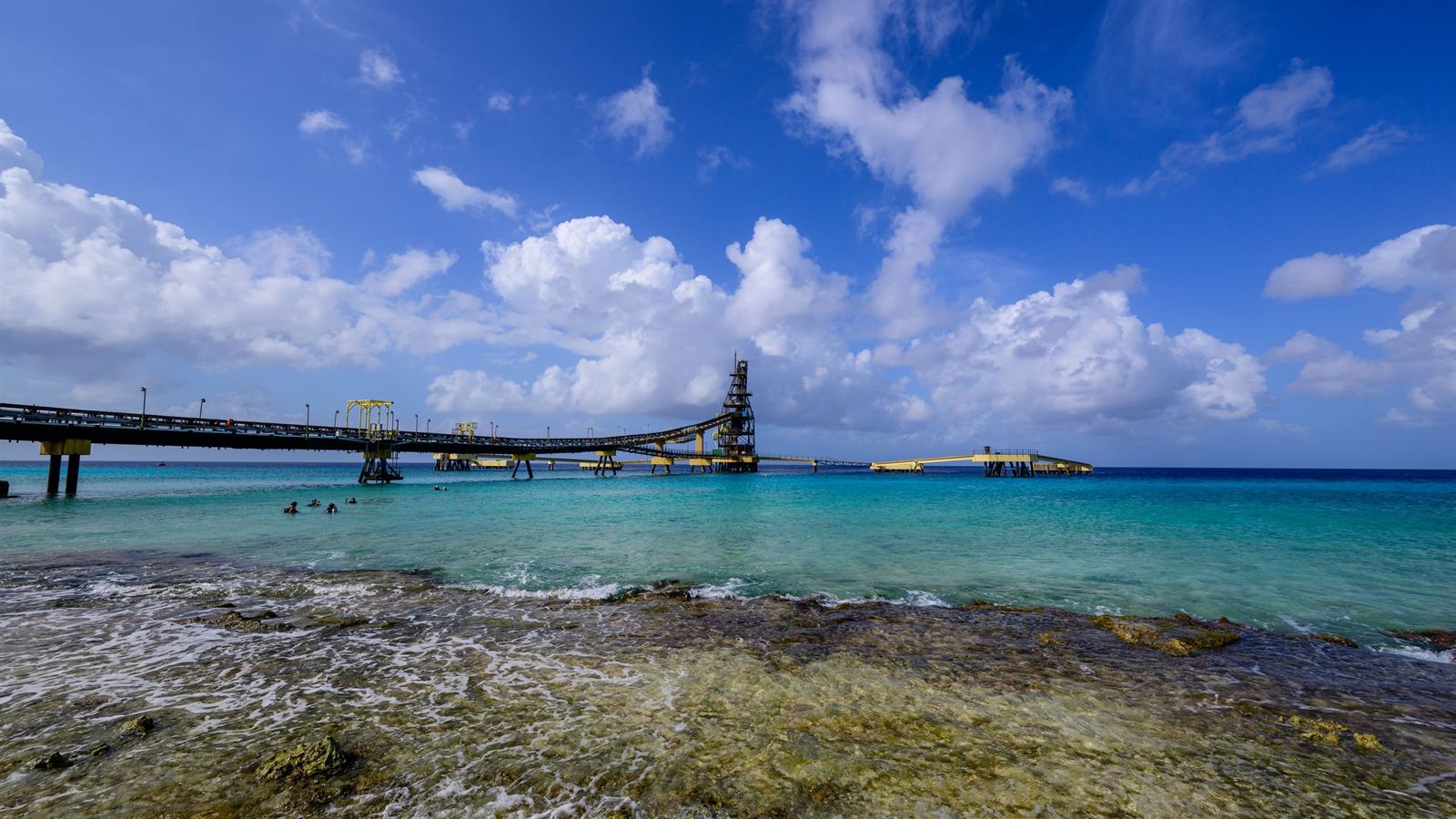 Long industrial salt pier stretching over turquoise Caribbean water beside a rocky shore on Bonaire