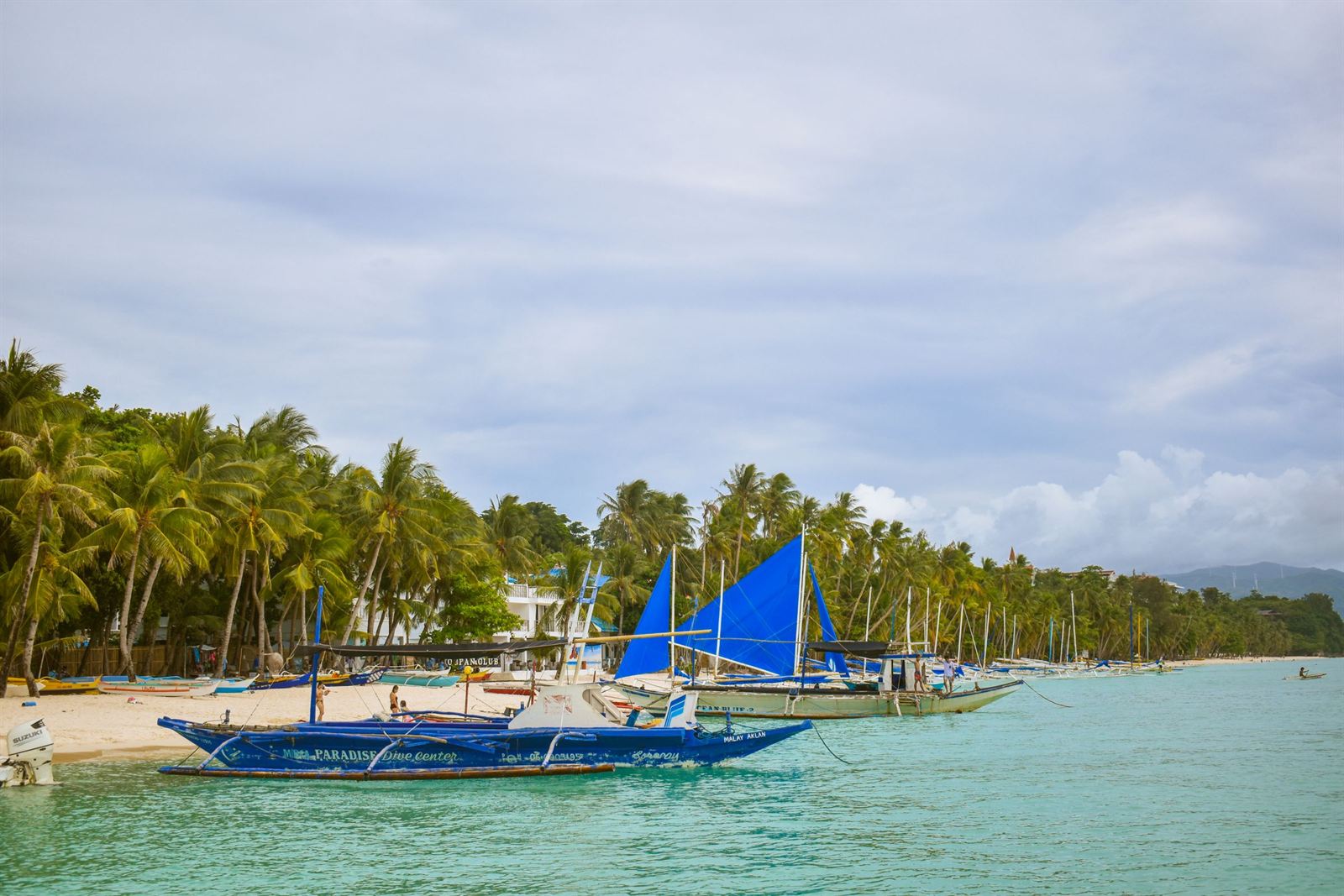 Paraw sailboats with blue sails on Boracay's White Beach lined with coconut palms and turquoise water