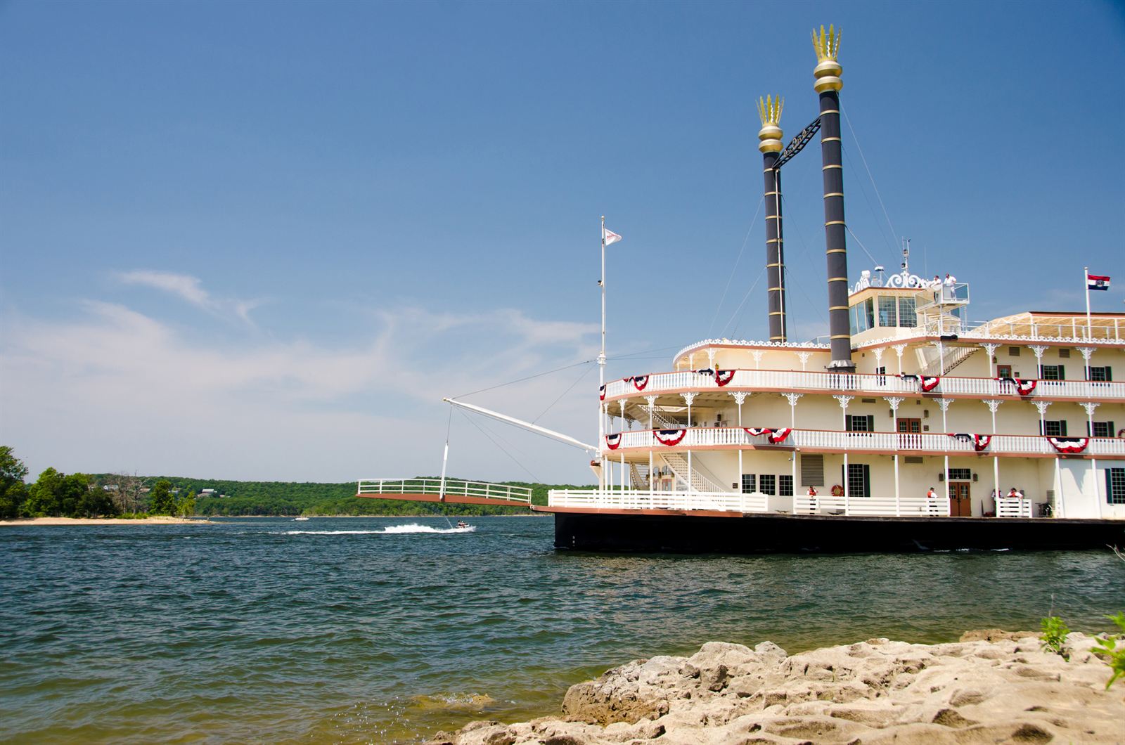 Branson Belle paddlewheel showboat with twin smokestacks docked on the lake under blue sky