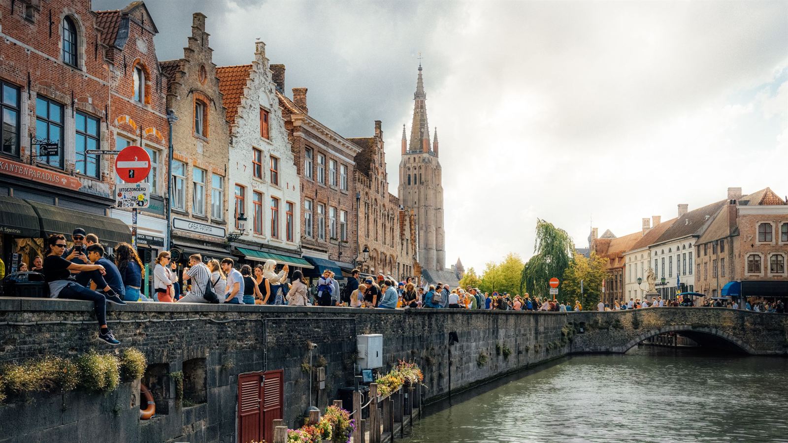 Bruges canal quay with stepped-gable houses, crowds on the bridge and the spire of the Church of Our Lady